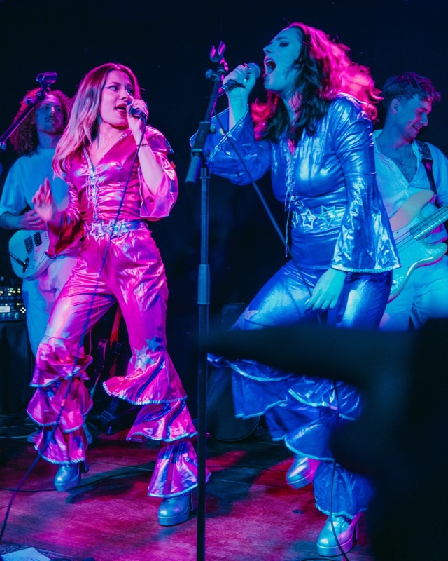 ABBA tribute band performing in vivid pink and blue costumes