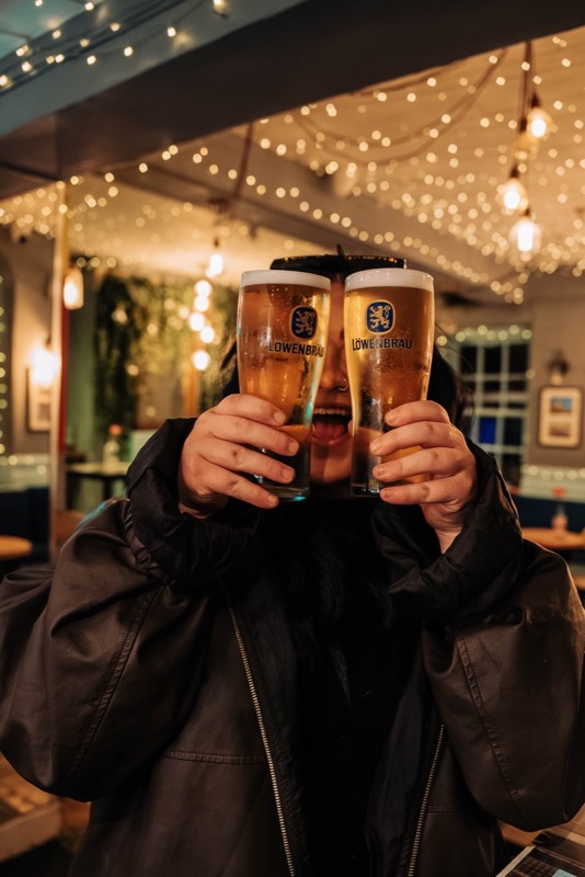 Two pints raised beneath warm fairy lights